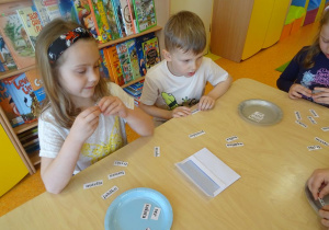 Dwójka dzieci czyta nazwy produktów spożywczych zapisanych na karteczkach.